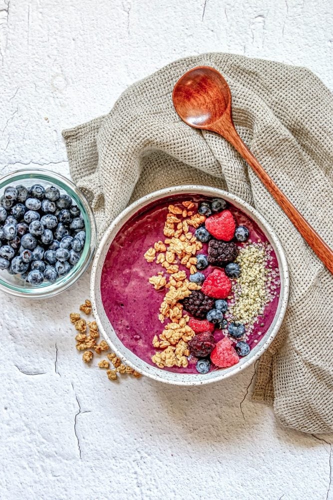 picture of berry smoothie bowl with raspberries, granola, blackberries, blueberries, and hemp hearts on top 