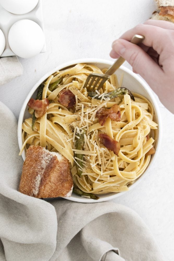 picture of a bowl with noodles, asparagus, parmesan cheese, bacon, and carbonara sauce