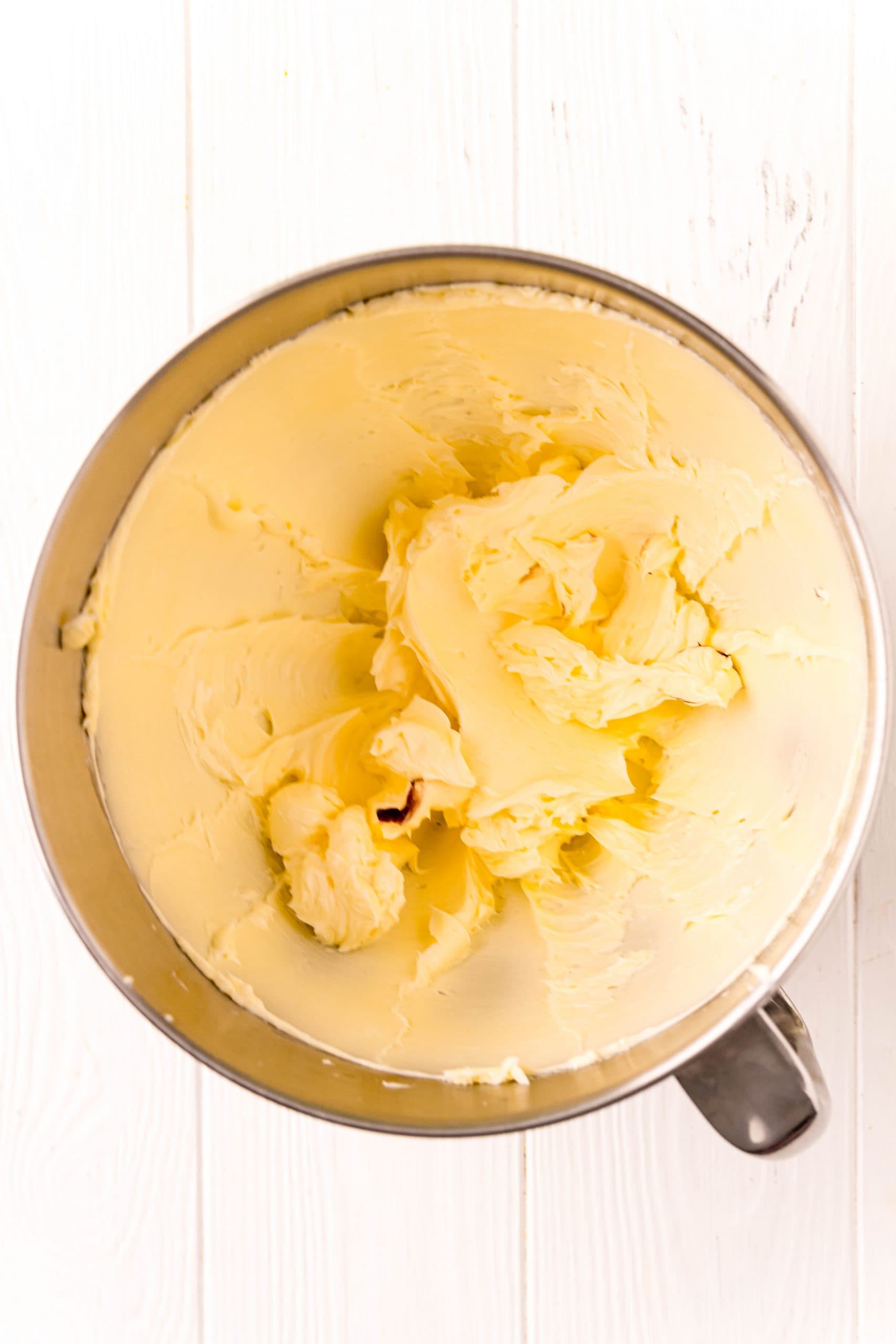 A delectable chocolate frosting recipe with butter in a metal bowl on a white wooden table.
