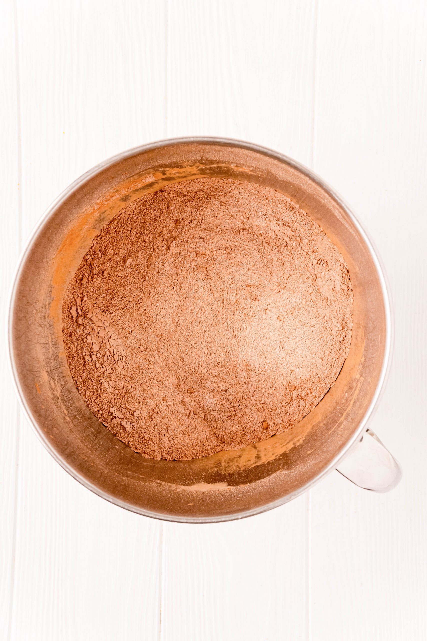 A metal bowl filled with brown powder for The Best Easy Chocolate Cake Recipe on a white background.