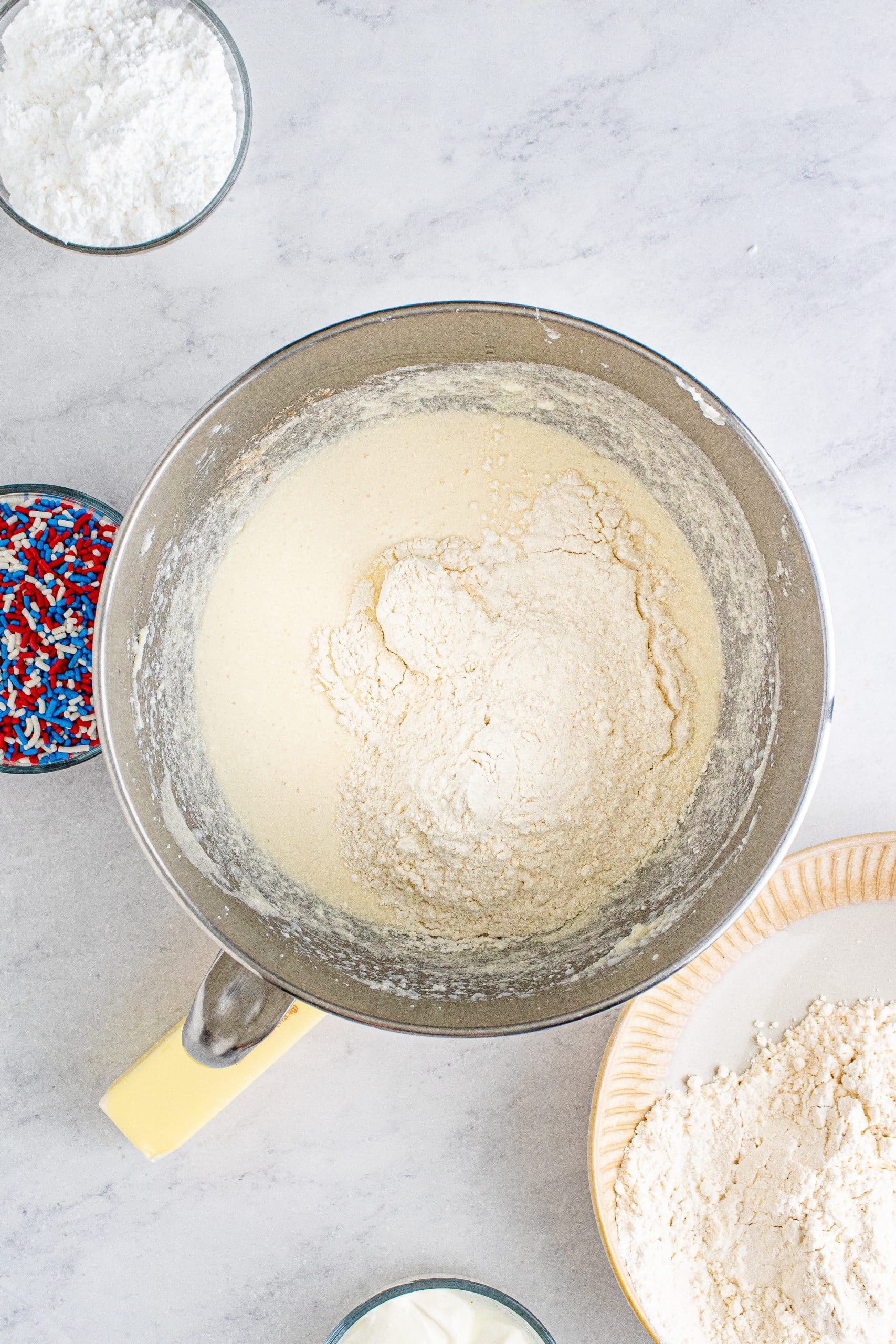 picture of flour dumped over wet cake ingredients in a bowl