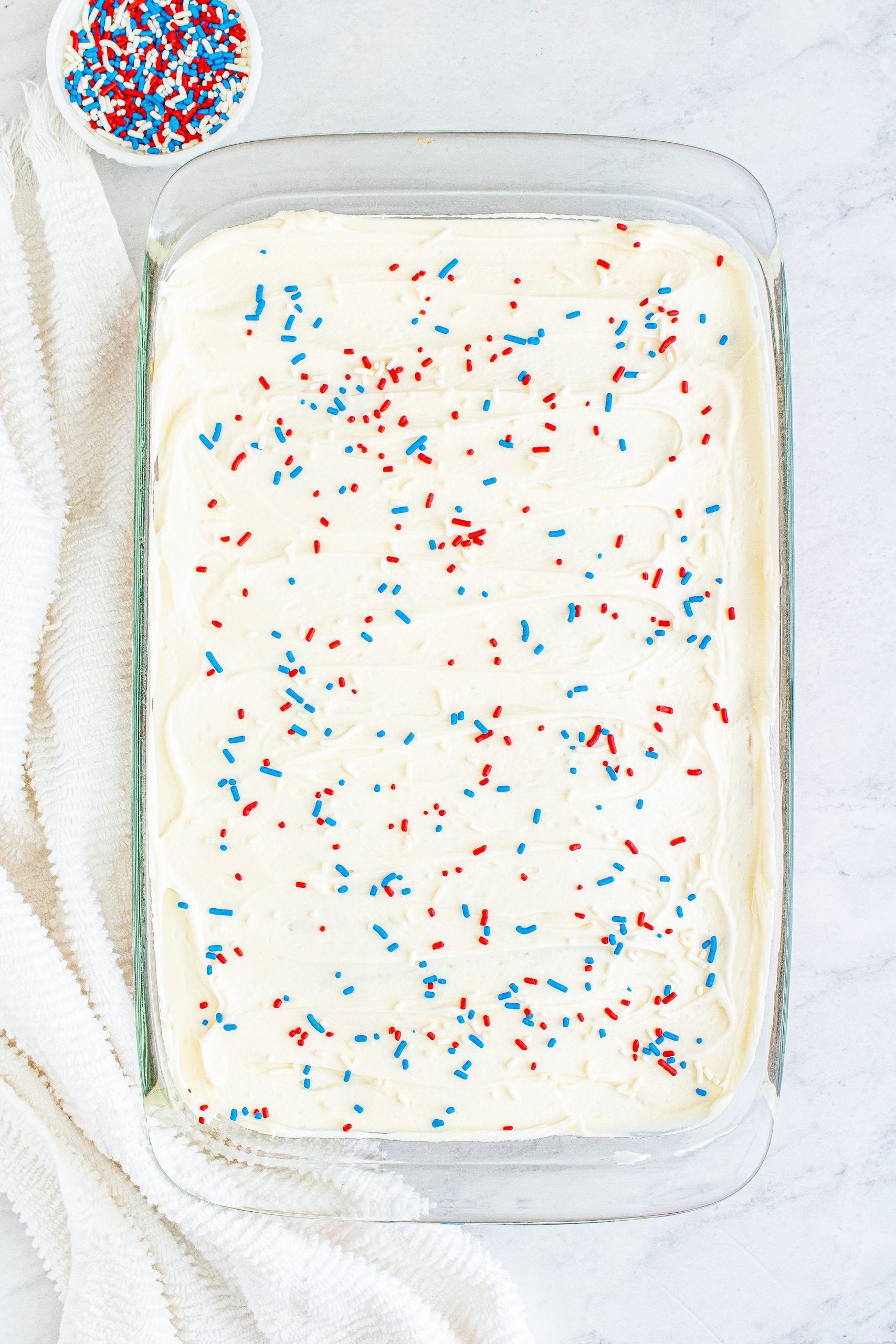 red white and blue sprinkles over iced sheetcake in a pan