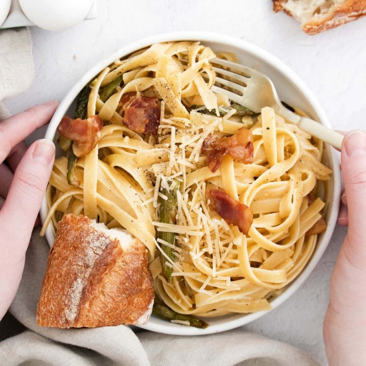picture of hand holding bowl of asparagus carbonara pasta