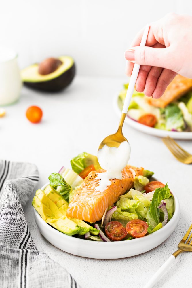 salad with avocado and tomatoes with salon on it and dressing