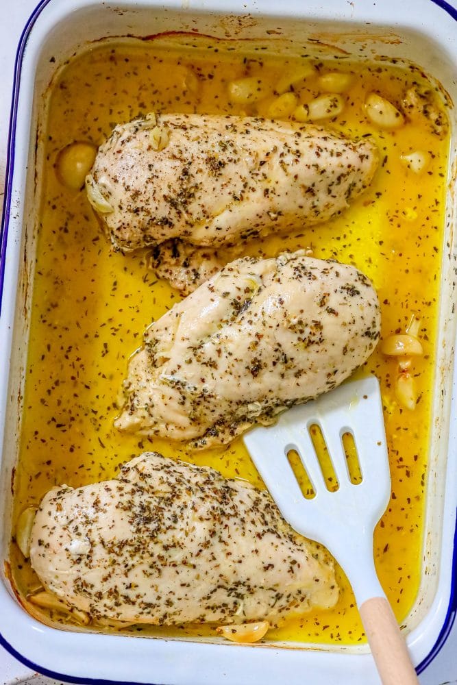 picture of spatula scooping up baked chicken breast from a pan with lemon juice and olive oil 