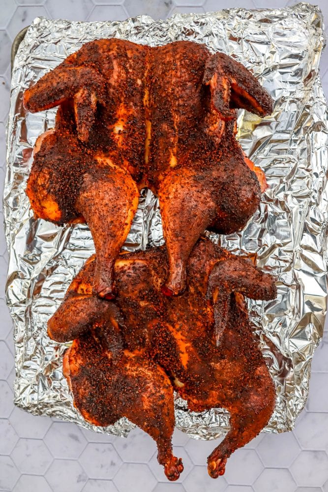  two spatchcocked smoked chickens on a baking sheet lined with tinfoil
