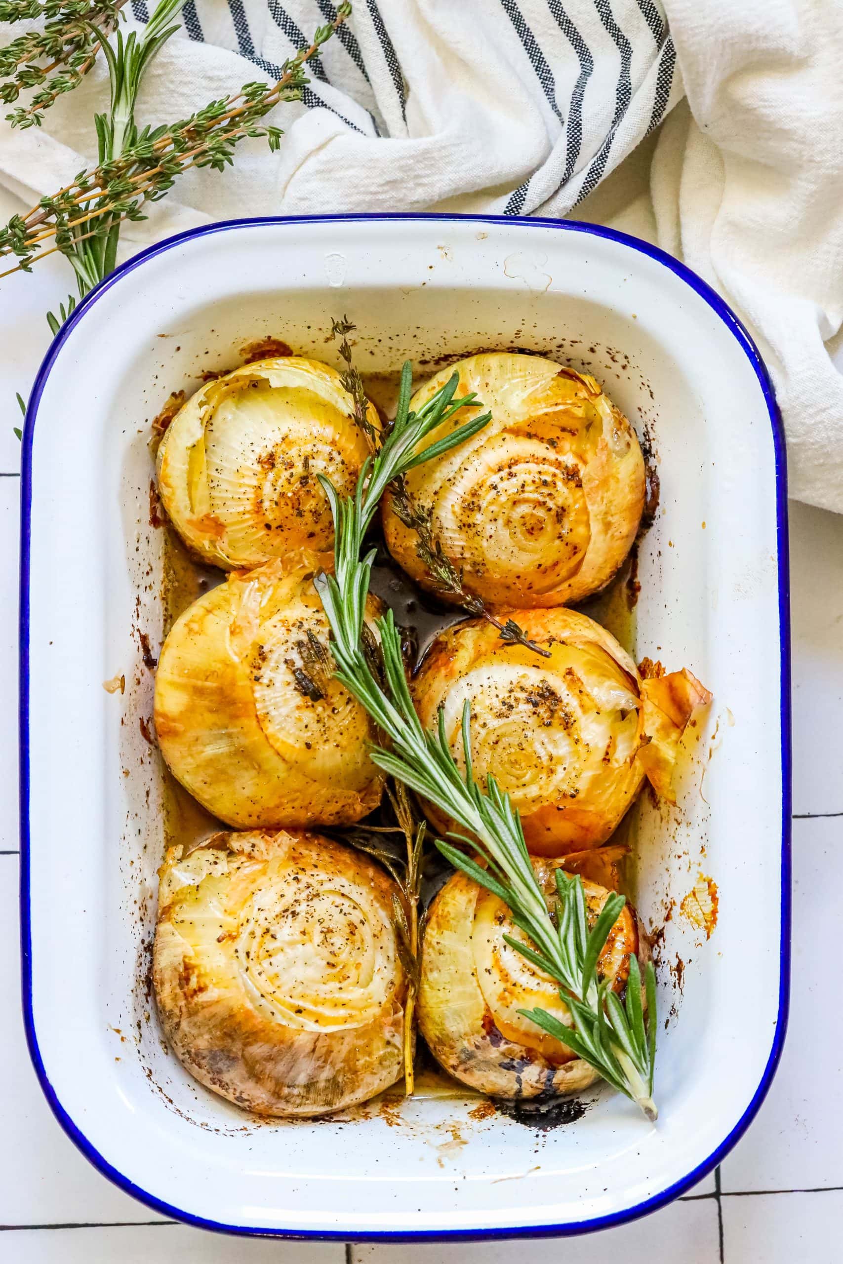 Roasted artichokes in a baking dish with rosemary sprigs and easy roasted onions.