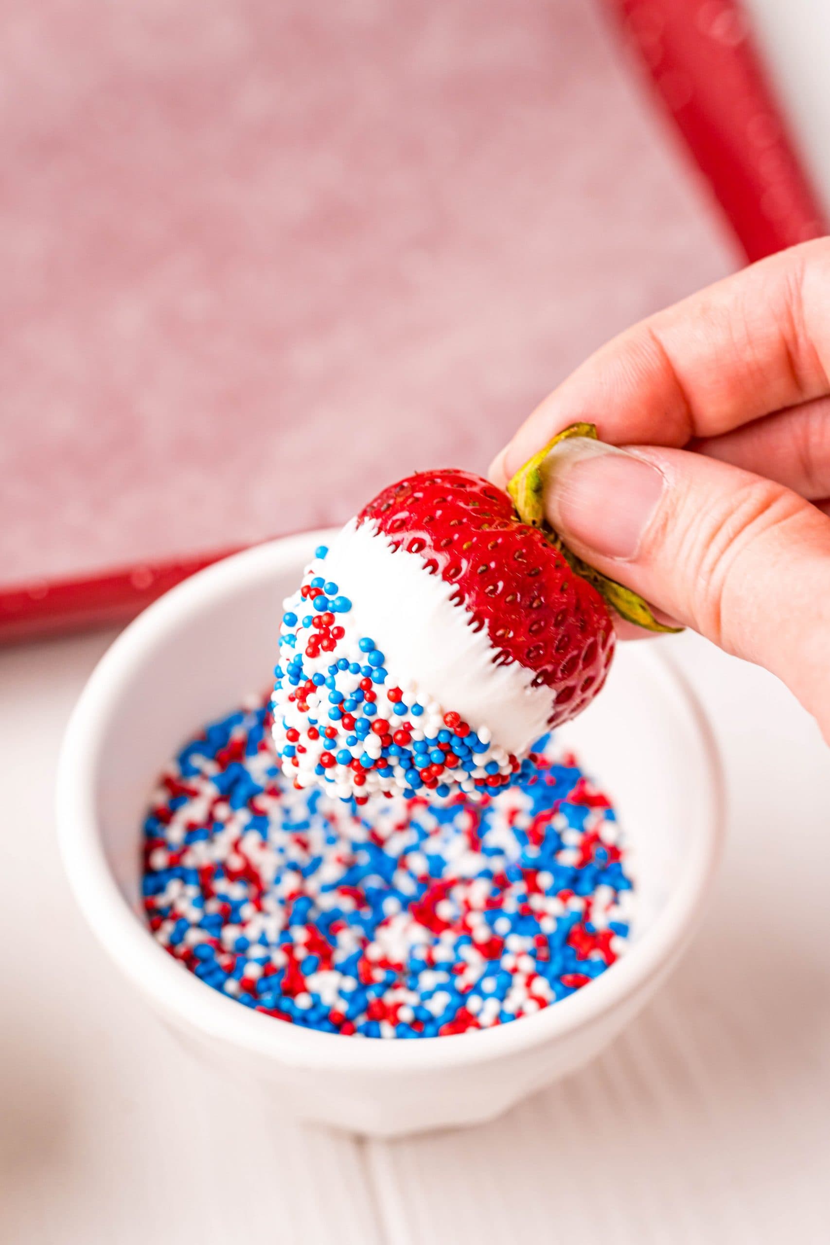 picture of a strawberry with melted white chocolate being dipped into sprinkles