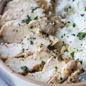 Sliced baked garlic lemon chicken breast, garnished with herbs, served next to white rice in a bowl.