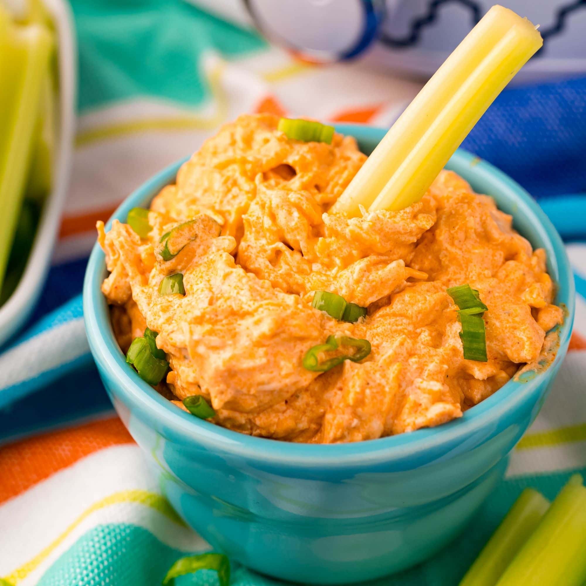 Buffalo chicken dip served in a blue bowl alongside celery sticks.