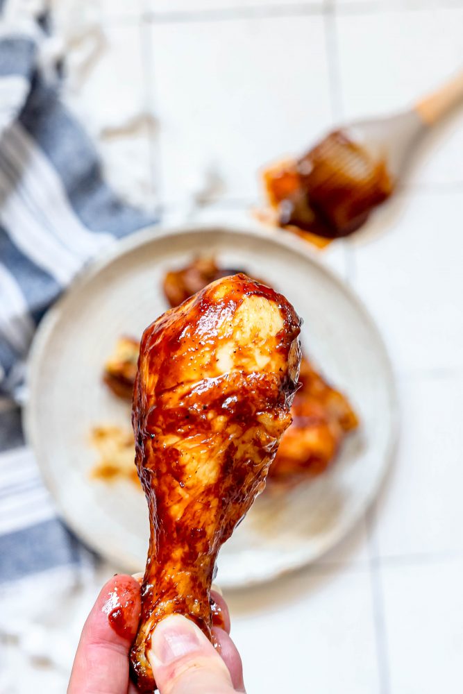 picture of a hand holding a chicken drumstick covered in bbq sauce 