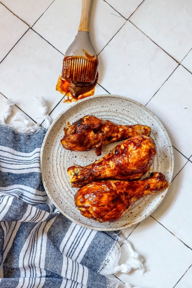 picture of air fried bbq chicken drumsticks on a white plate covered in bbq sauce