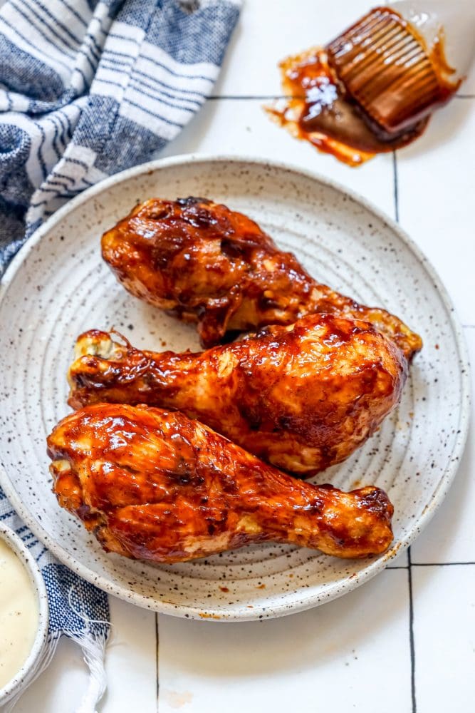 picture of air fried bbq chicken drumsticks on a white plate covered in bbq sauce