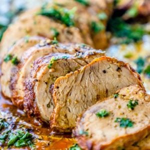 picture of sliced baked pork tenderloin topped with parsley on aluminum foil