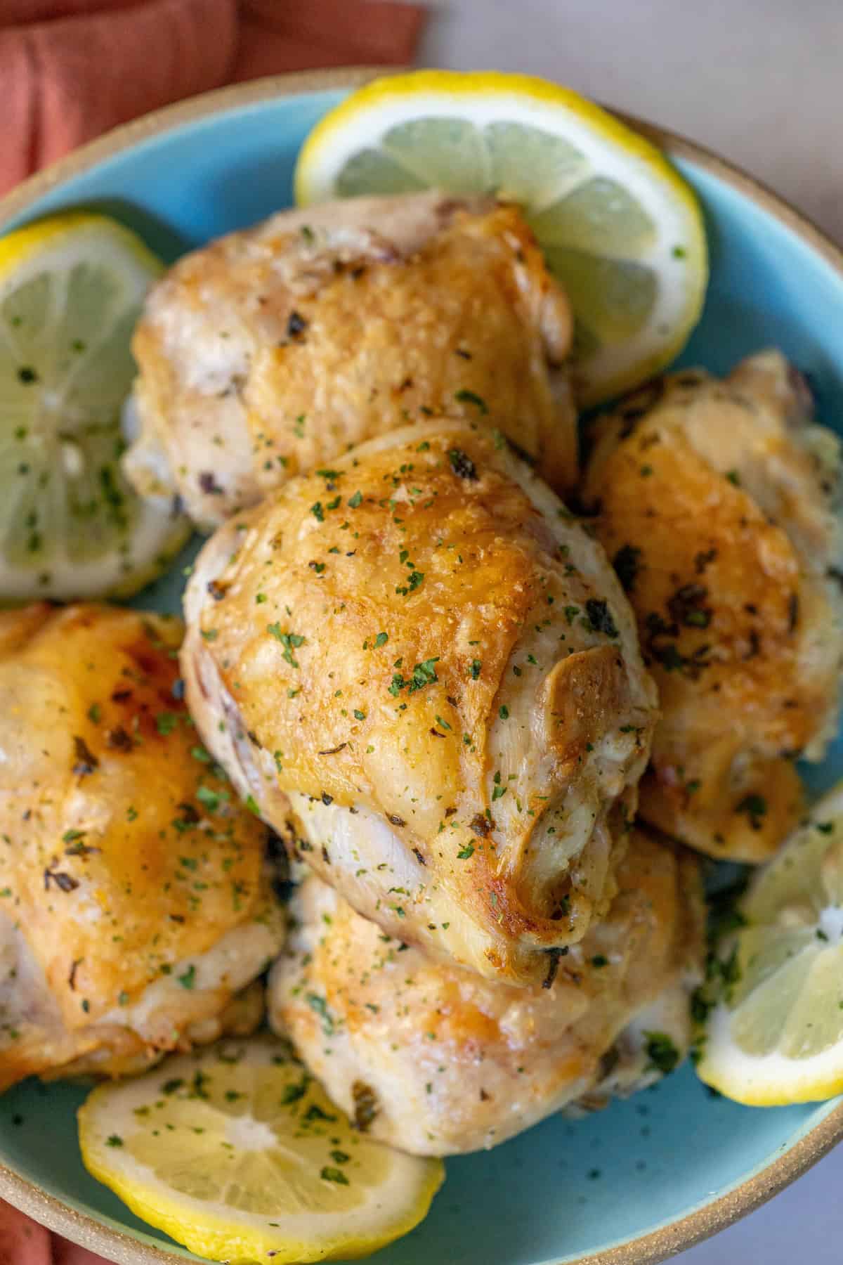 A blue plate showcases Easy Air Fried Lemon Chicken, with golden brown thighs garnished with chopped herbs and lemon slices.