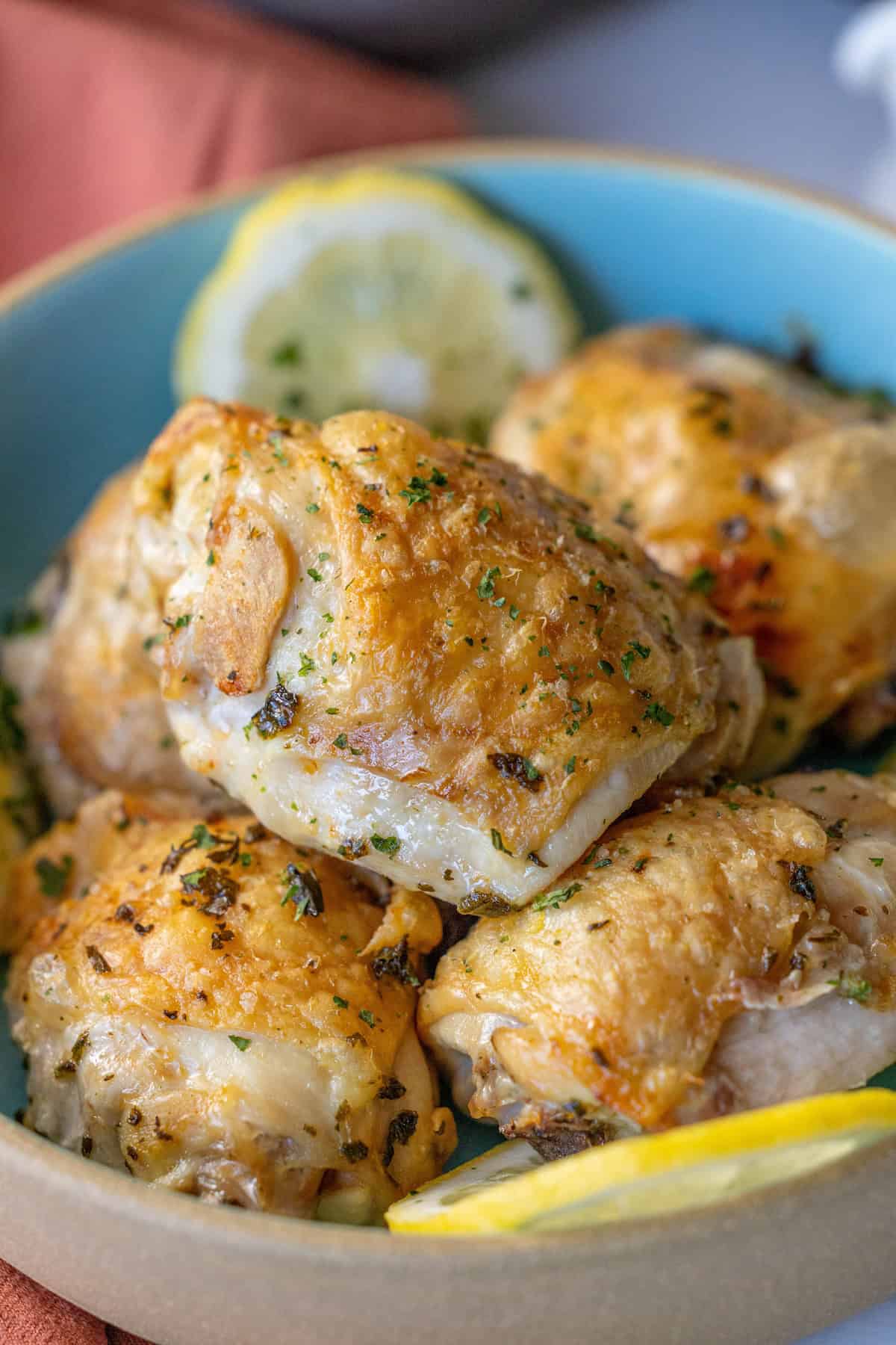 A bowl of golden brown roasted chicken pieces garnished with herbs, complemented by fresh lemon slices nearby—a delightful take on an easy air fryer lemon chicken recipe.