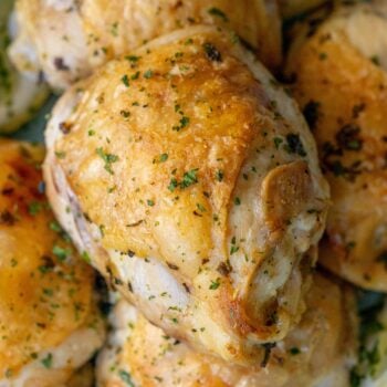 A close-up of golden-brown air fried lemon chicken thighs garnished with chopped herbs.