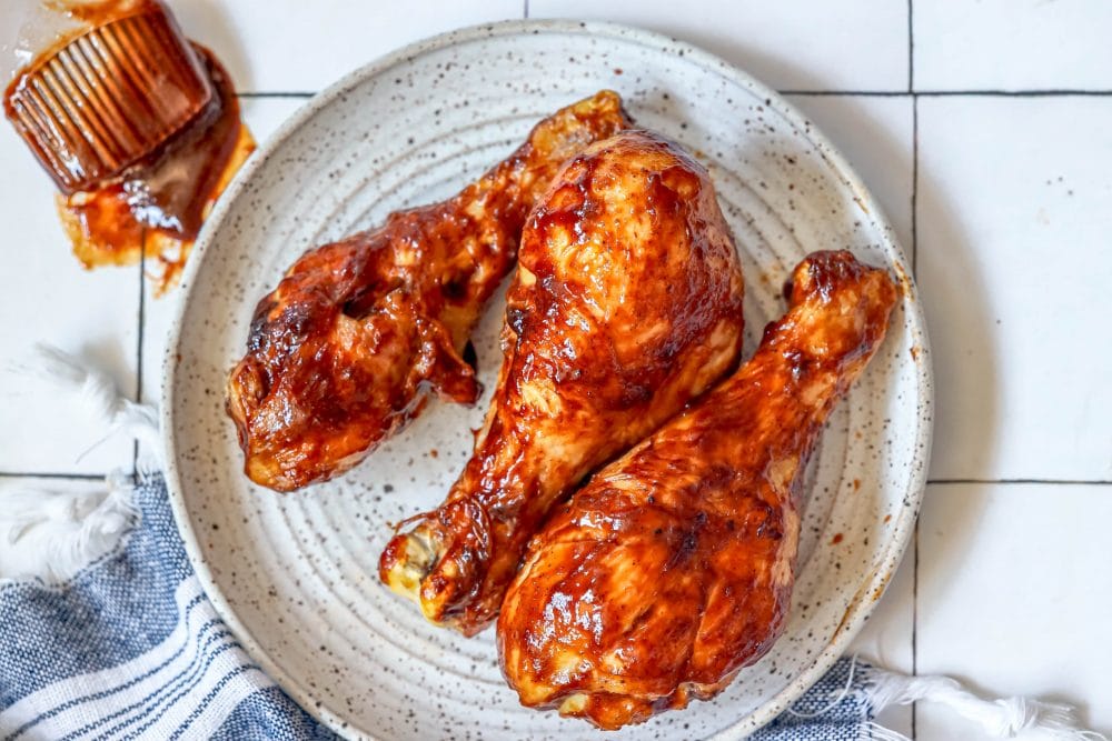 picture of air fried bbq chicken drumsticks on a white plate covered in bbq sauce