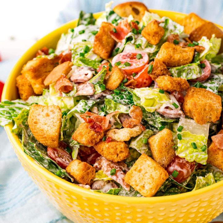 Caesar salad with croutons, bacon, and tomato in a yellow bowl.
