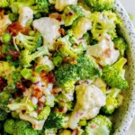 picture of broccoli and cauliflower salad in a speckled bowl with bacon and peas