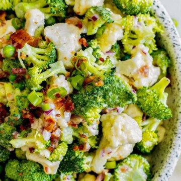 picture of broccoli and cauliflower salad in a speckled bowl with bacon and peas