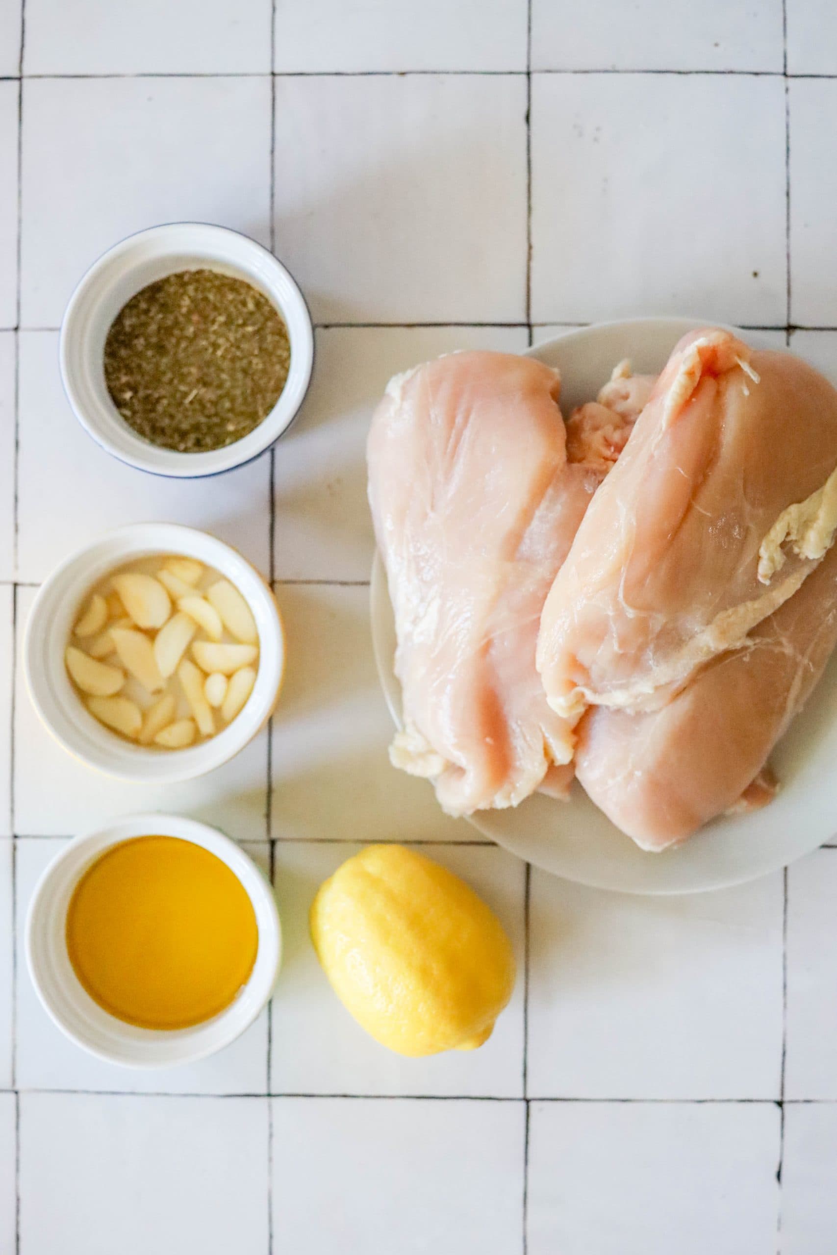 Baked chicken breasts with lemon and garlic ingredients on a white tiled floor.