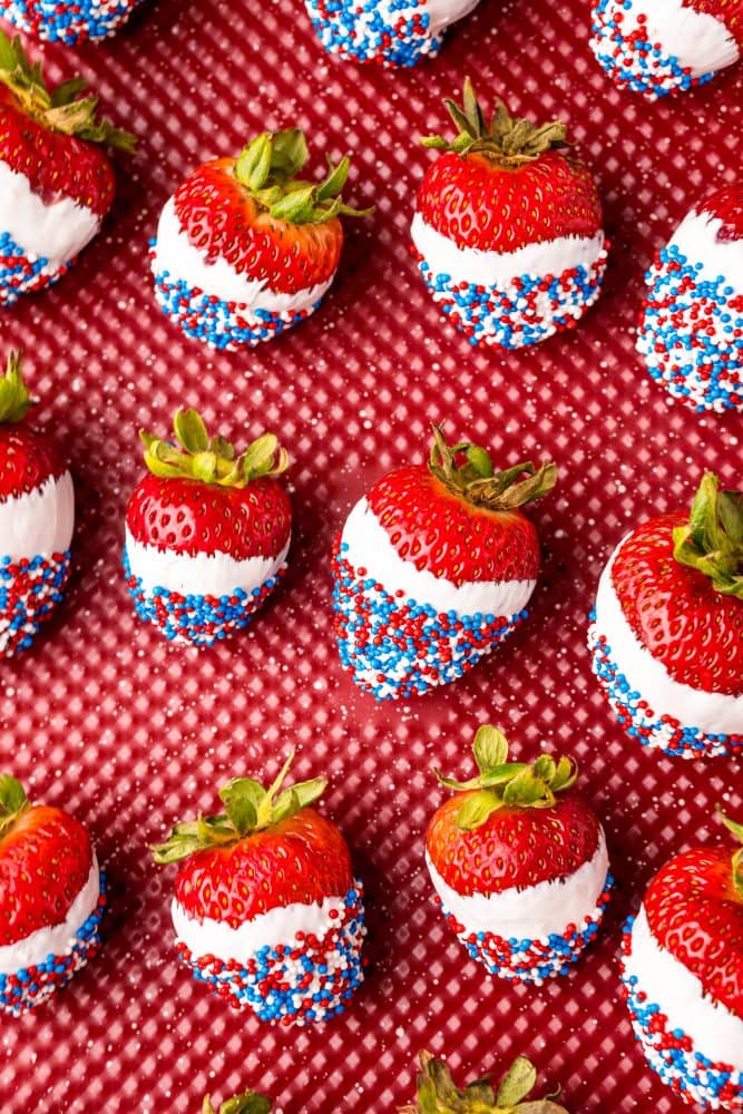 picture of red white and blue sprinkle dipped white chocolate strawberries on a red plate