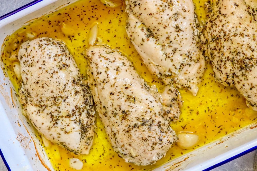 chicken breasts in white baking dish with melted butter, lemon juice, herbs, and garlic