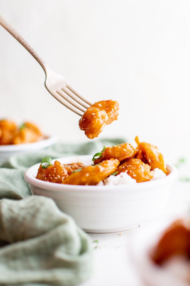 picture of sesame chicken on a fork over a bowl of rice