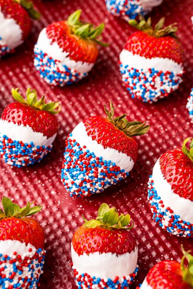 picture of red white and blue sprinkle dipped white chocolate strawberries on a red plate