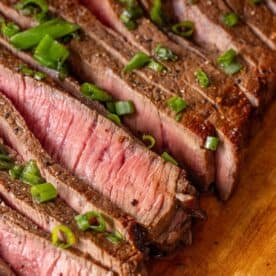 Sliced medium-rare steak on a cutting board, topped with chopped green onionsโjust like the best air fryer London broil recipe.