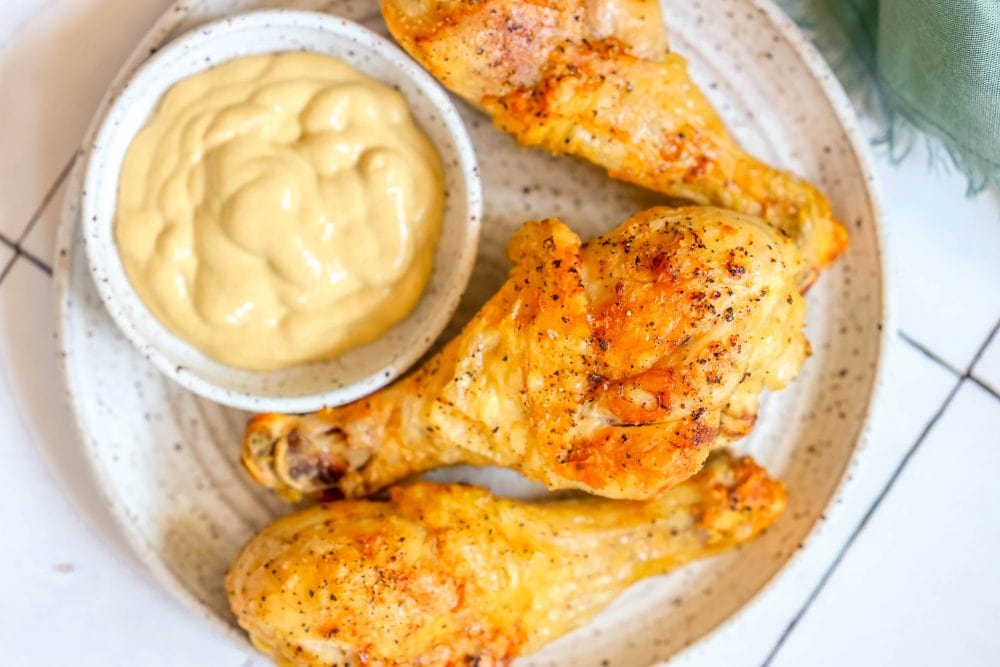 picture of 3 chicken drumsticks on a plate with a small bowl of mustard sauce next to them