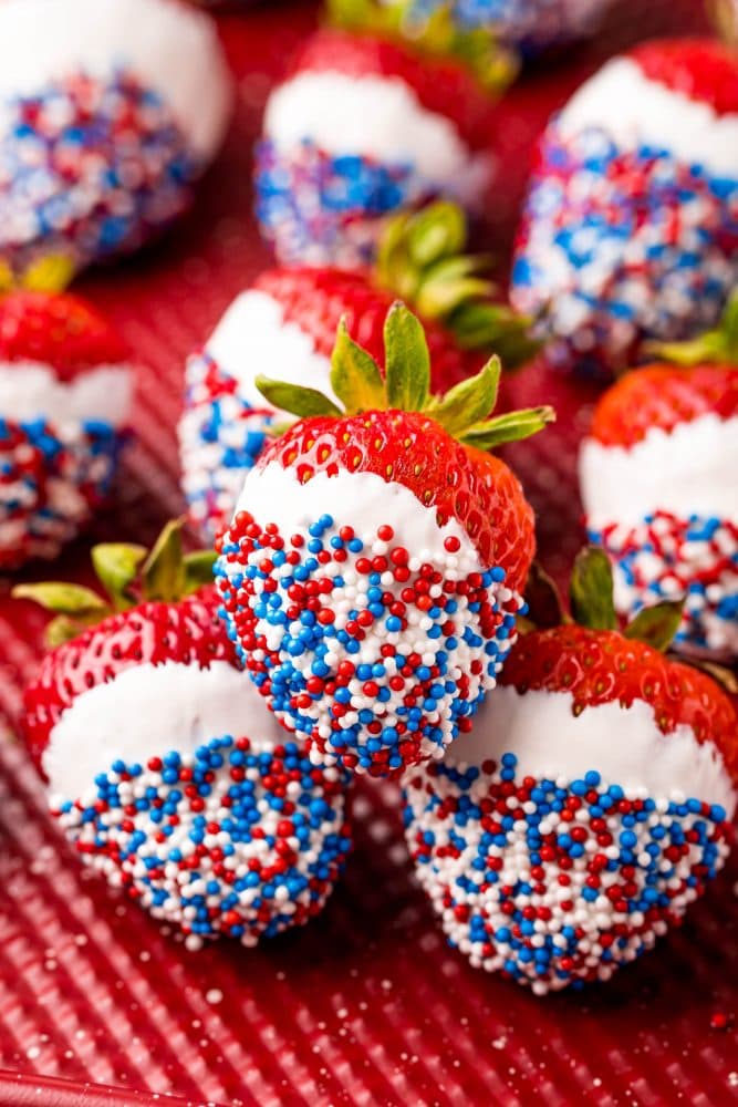 picture of red white and blue sprinkle dipped white chocolate strawberries on a red plate