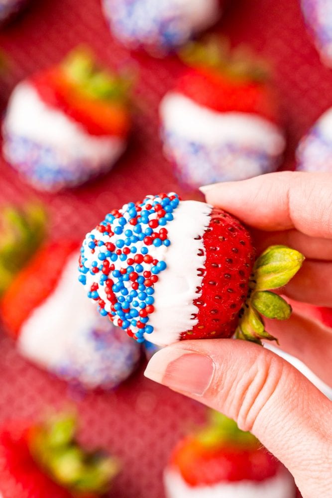 picture of a hand holding a strawberry dipped in white chocolate and covered in red white and blue sprinkles