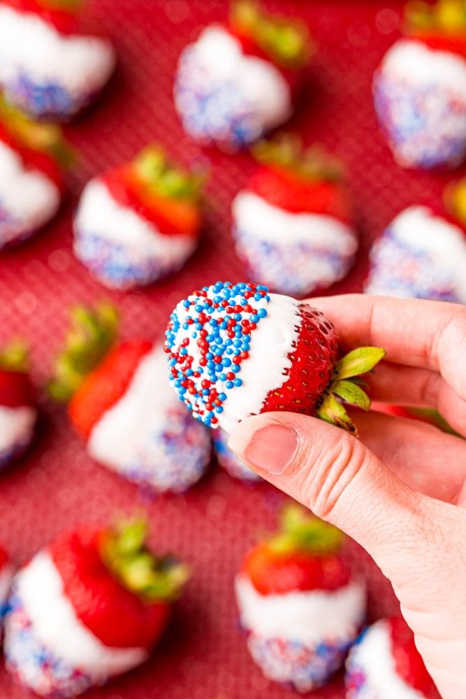 picture of a hand holding a strawberry dipped in white chocolate and covered in red white and blue sprinkles