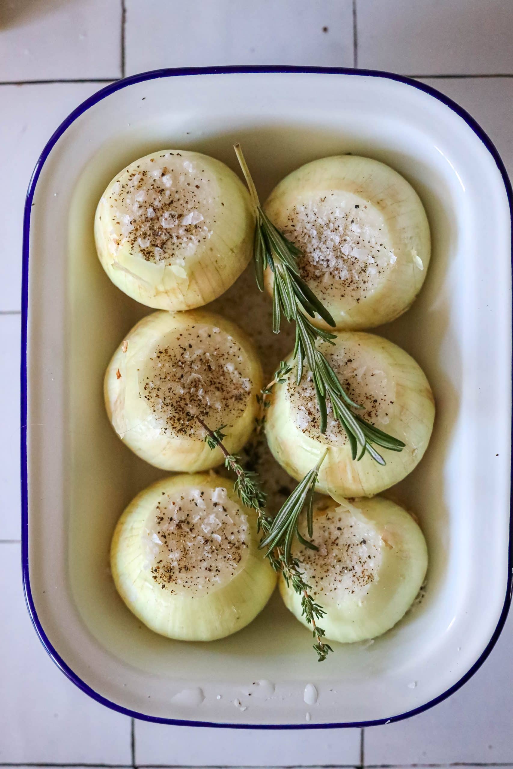 picture of whole onion with the top cut off and seasonings on top in a baking dish