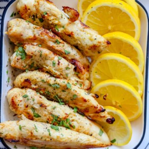 naked chicken tenders in a white dish with lemon slices next to them