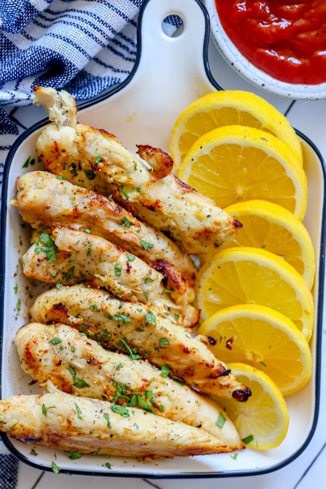 browned chicken tenders without breading in a white dish with lemon slices next to them