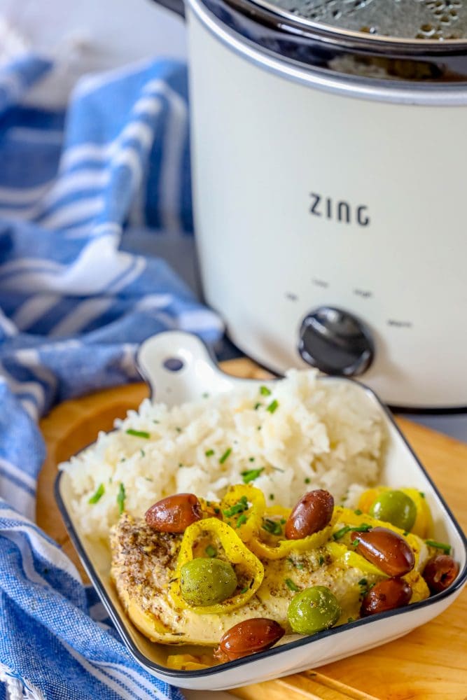 picture of chicken breast with olives and pepperoncinis in a white dish with rice in front of a slow cooker