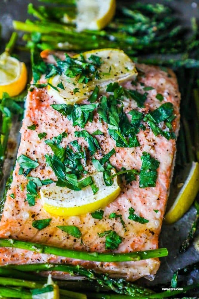 picture of salmon and asparagus on a baking sheet with lemons and parsley on top of it