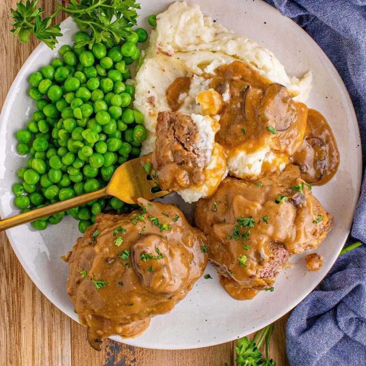 picture of salisbury steaks on a plate with mashed potatoes and peas