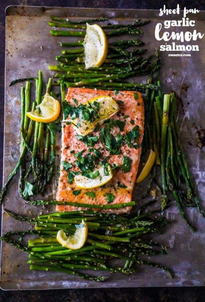 picture of salmon and asparagus on a sheetpan with slices of lemon and parsley sprinkled on top