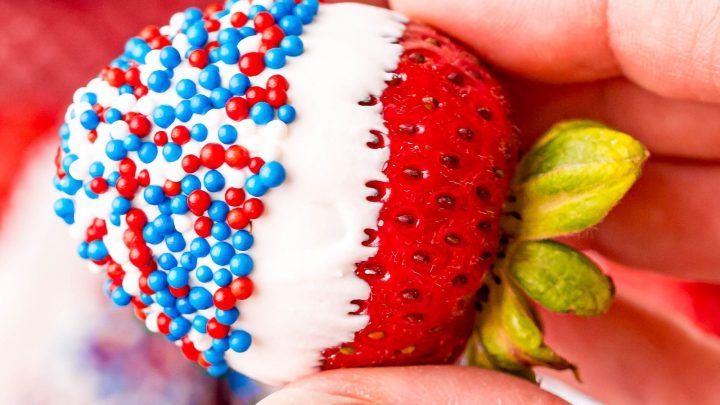 picture of a hand holding a strawberry dipped in white chocolate and sprinkles