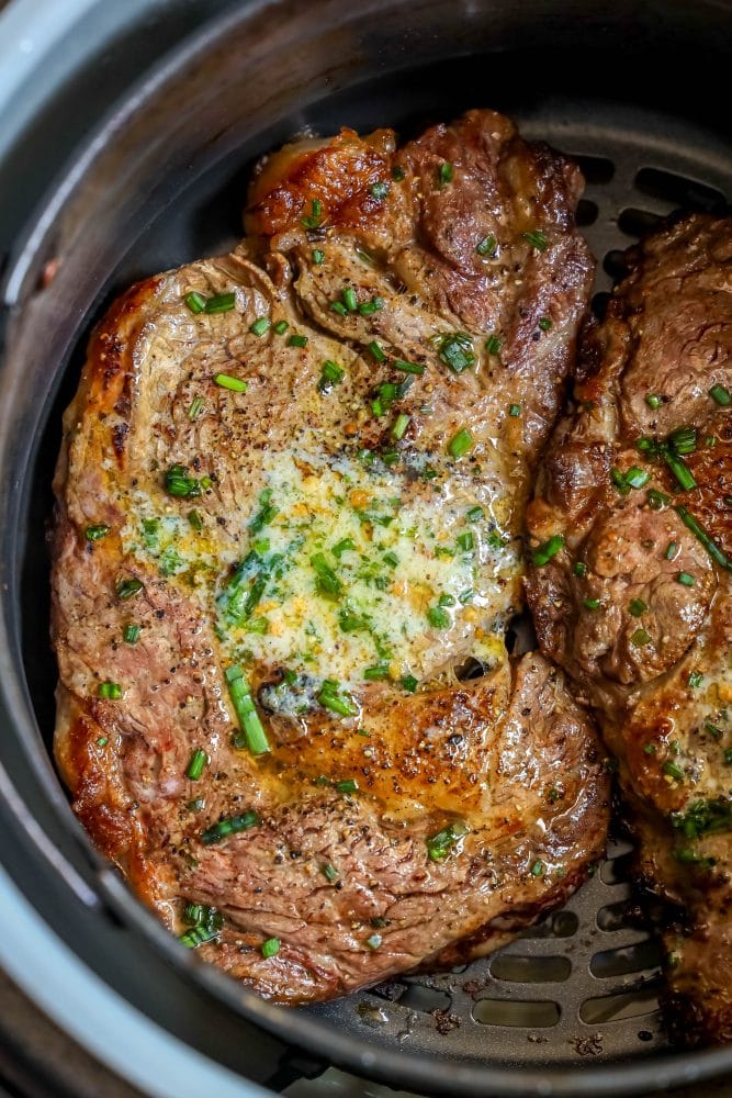 a steak in an air fryer basket with butter and chives on them