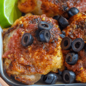 Close-up of air fried salsa chicken thighs topped with sliced black olives and tomato sauce, served with lime wedges.