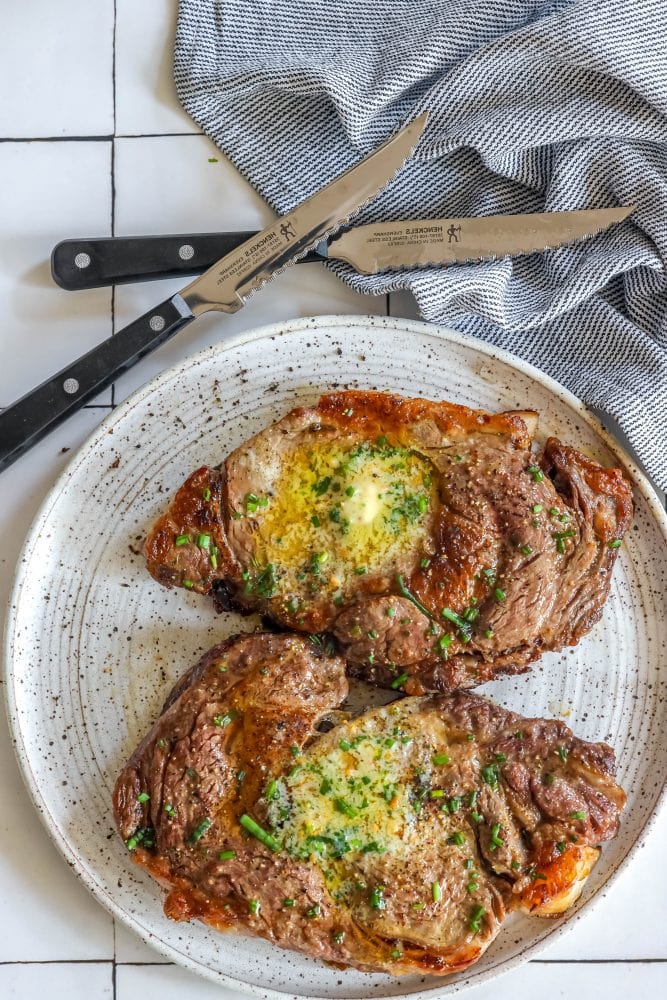 two steaks with butter and chives on them