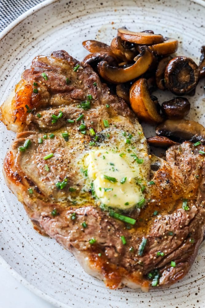 picture of ribeye steak on a plate with mushrooms and pats of butter on top