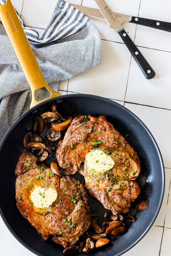 picture of ribeye steaks in a pan with mushrooms and pats of butter on top