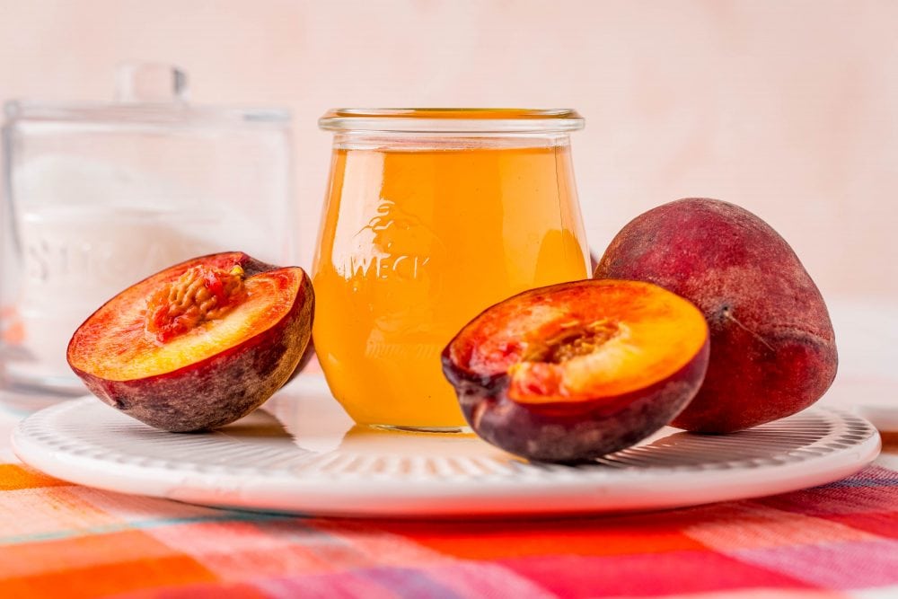 peaches cut in half next to a jar of peach syrup on a table