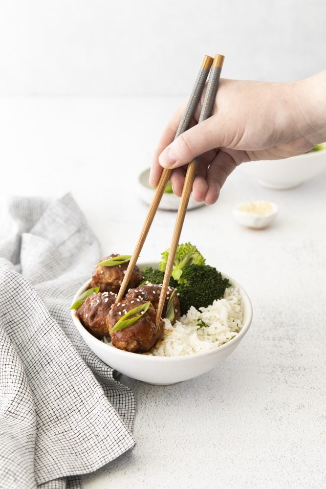 toothpicks picking up meatballs in sticky sauce with sesame seeds and green onions on it